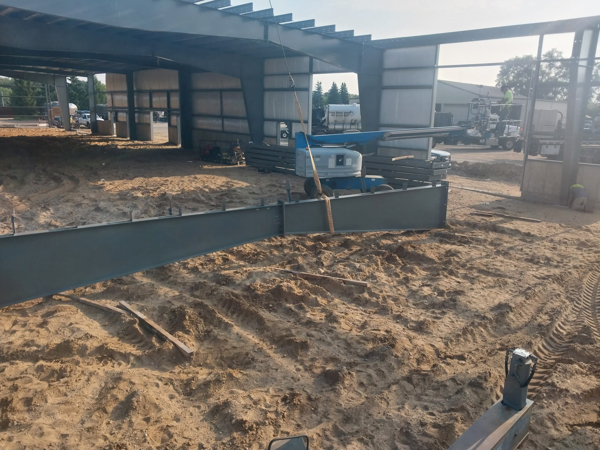 Construction site with metal beams and sand under a partially built structure.