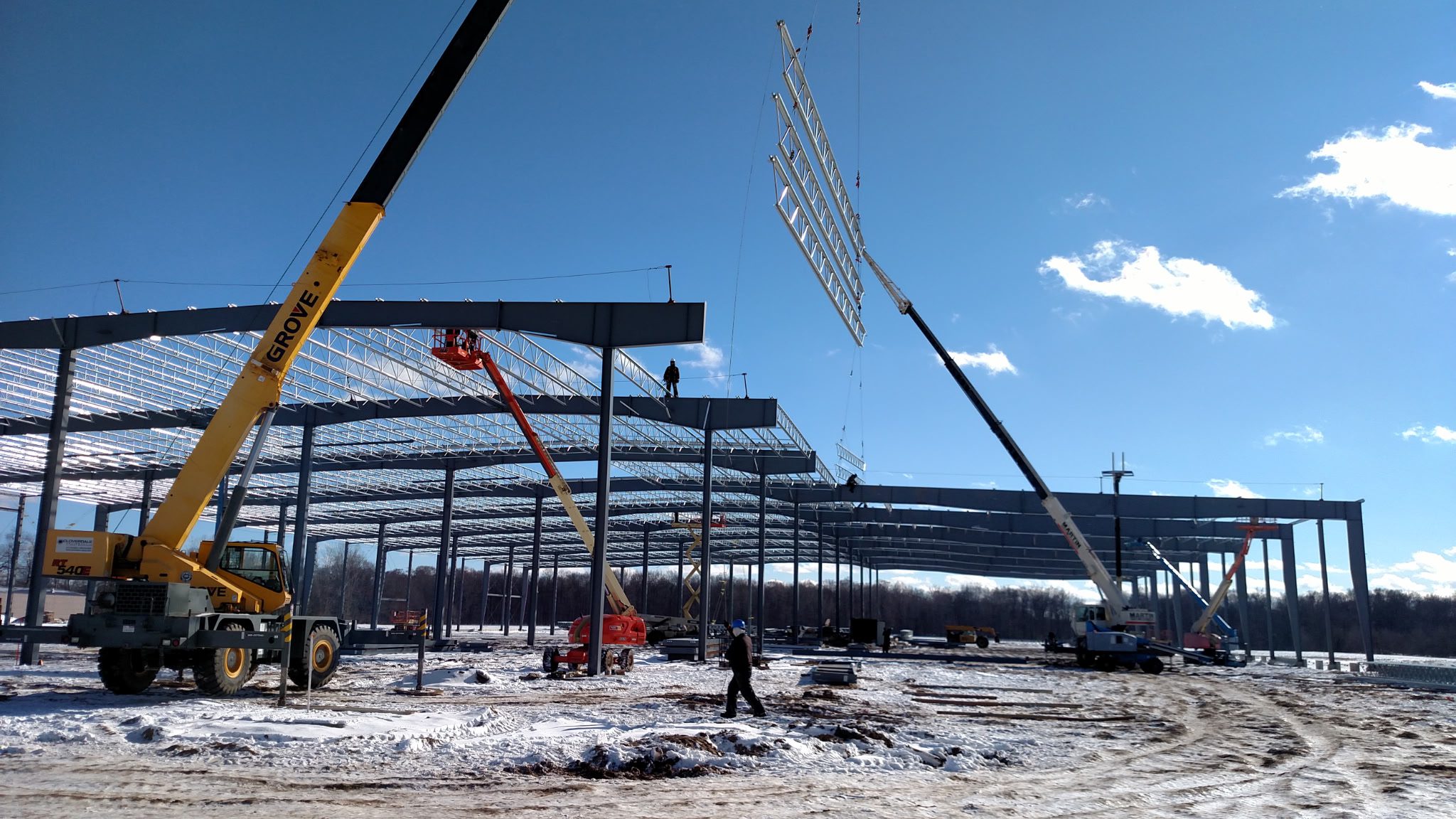 Steel framework being constructed at a snowy building site under a clear sky.
