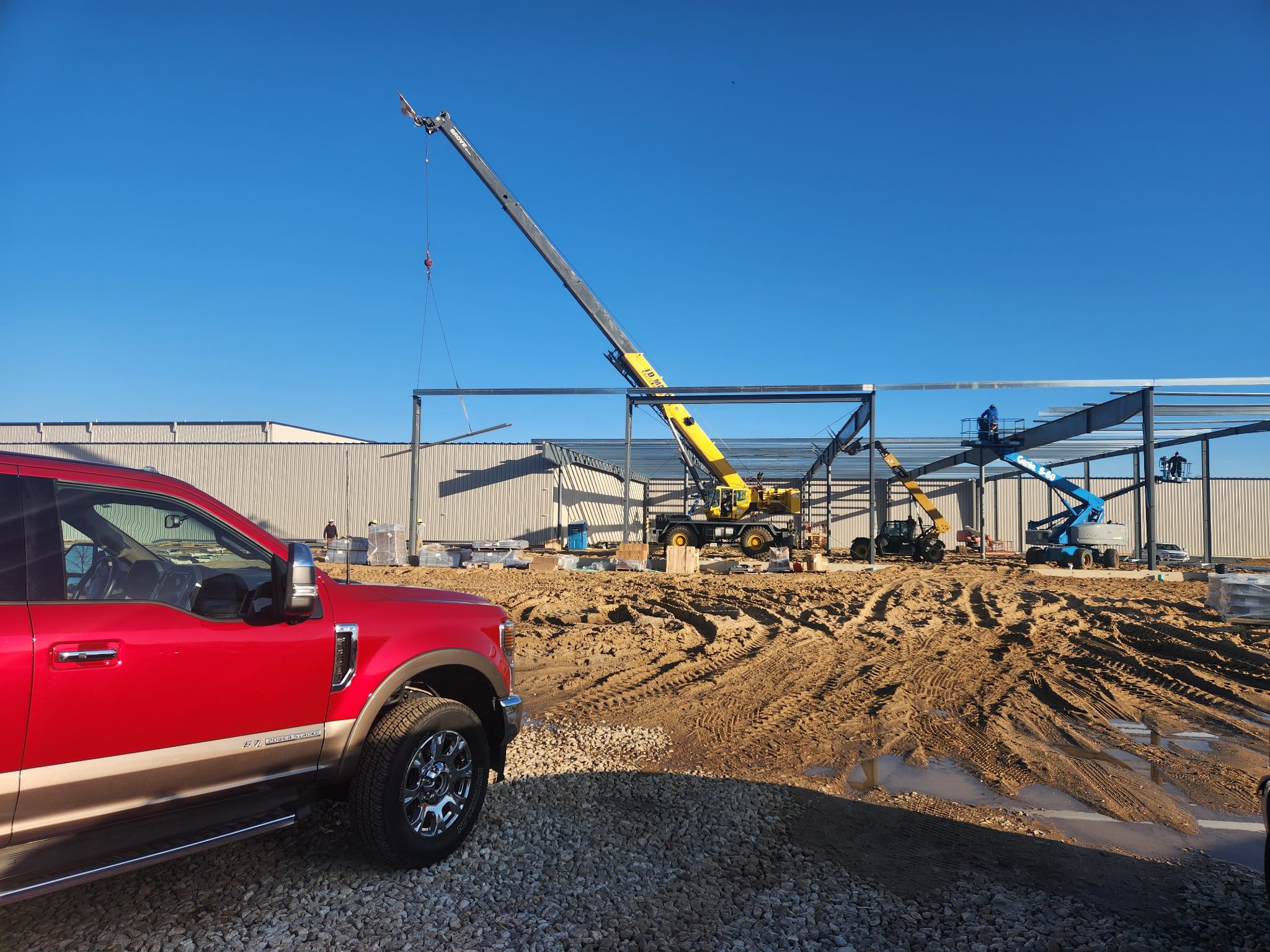 Construction site with a crane and a red truck under a clear blue sky.
