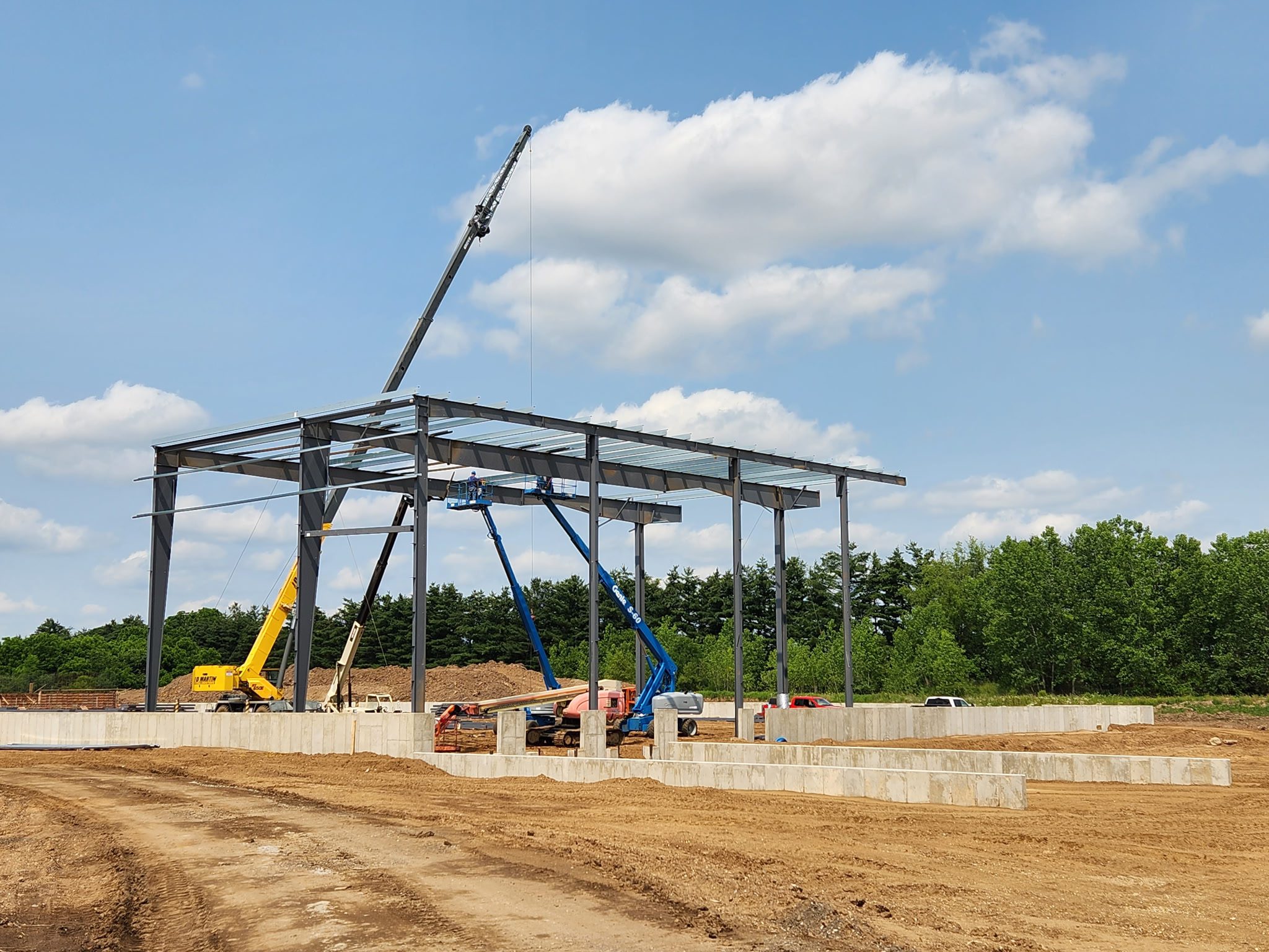 Steel framework being erected at a construction site under a partly cloudy sky.