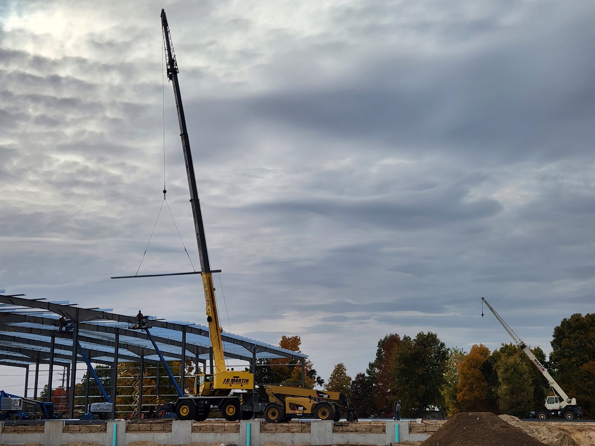 A crane lifting steel beams at a construction site on a cloudy day.