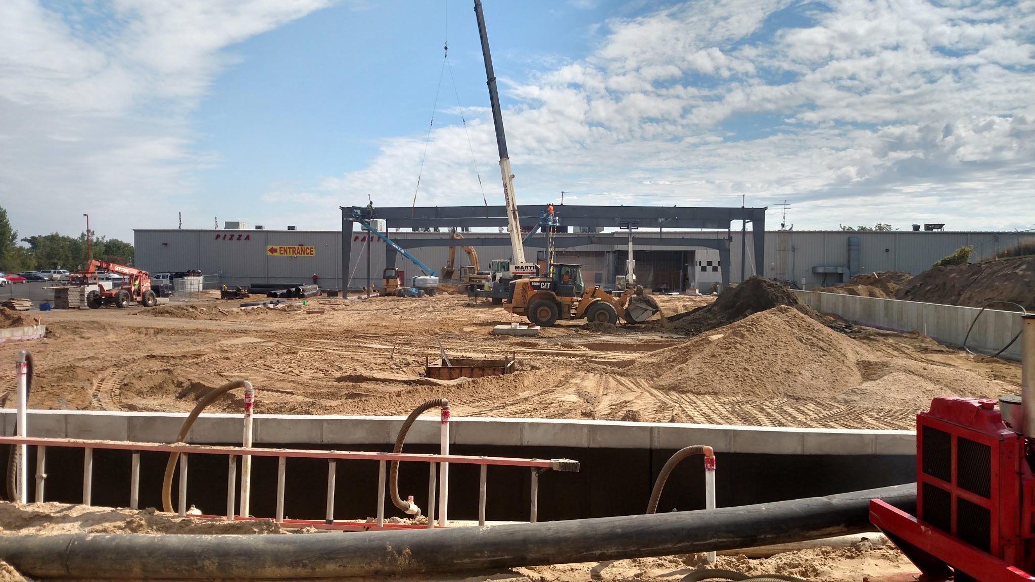 Construction site with steel framework and crane under a partly cloudy sky.