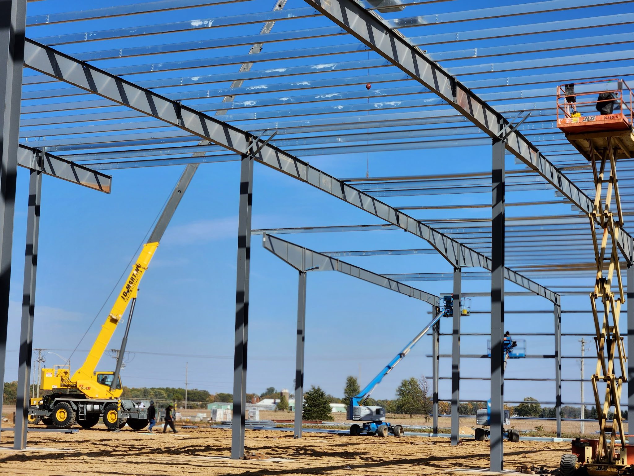 Steel framework being erected on a construction site under a clear sky.