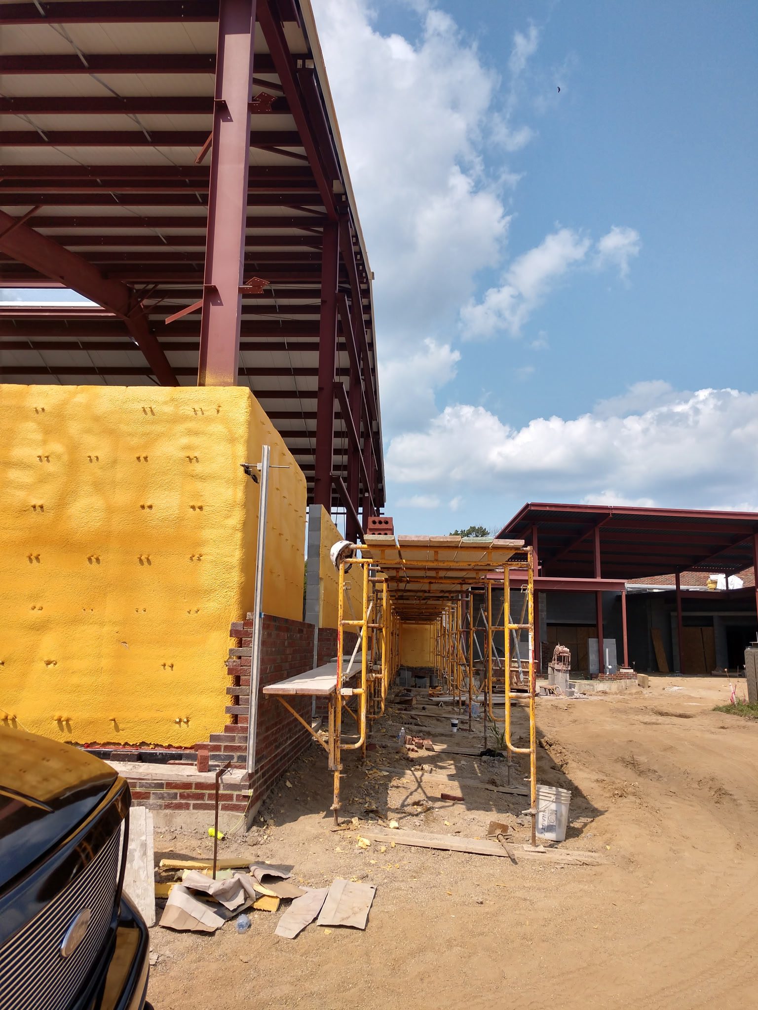 Construction site with steel beams and wooden panels under a partly cloudy sky.