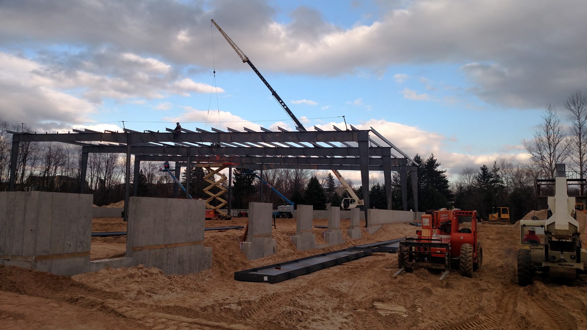 Construction site with steel framework and crane under a cloudy sky.