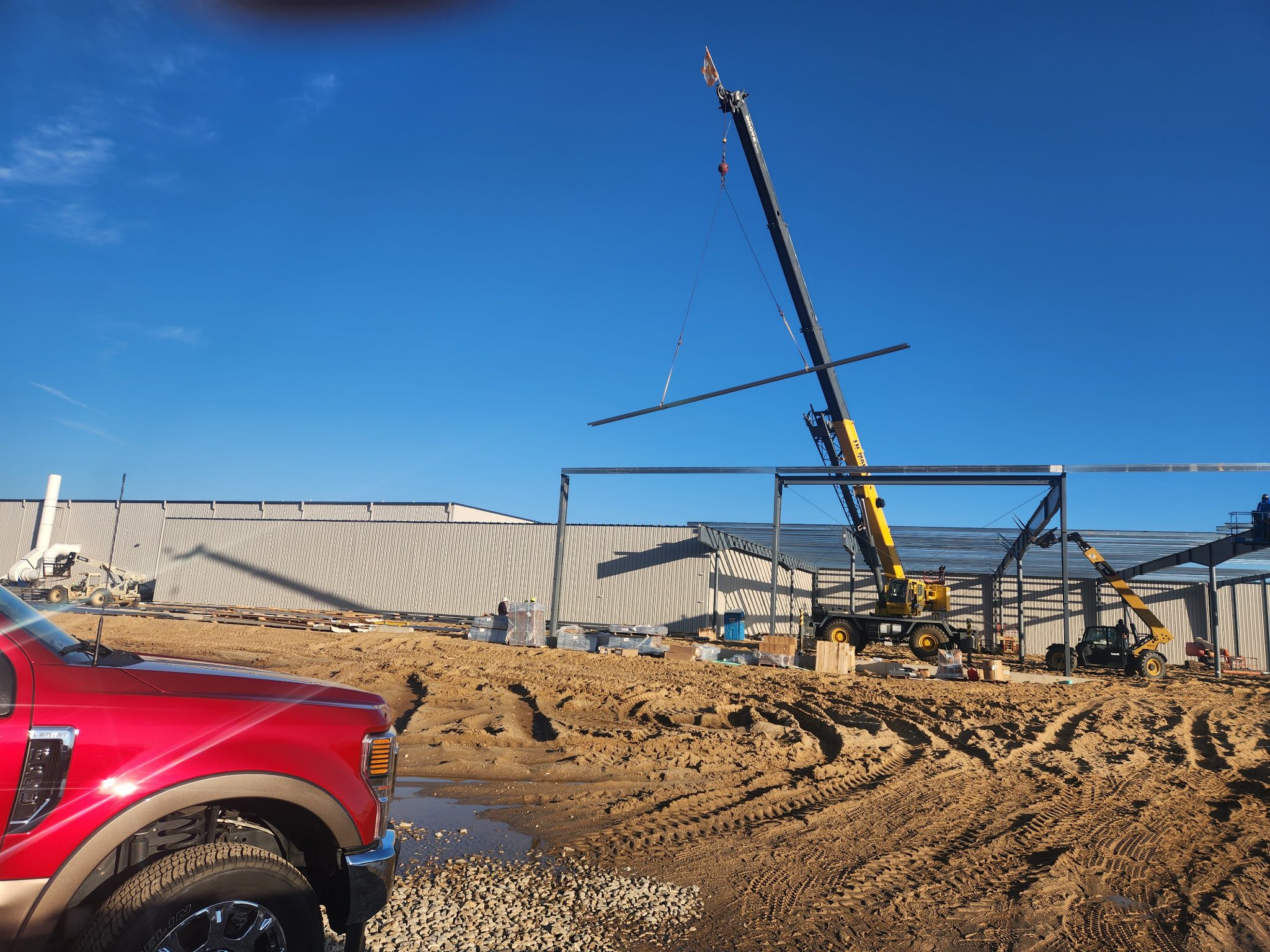 Crane lifting steel beams at a construction site under clear blue sky.