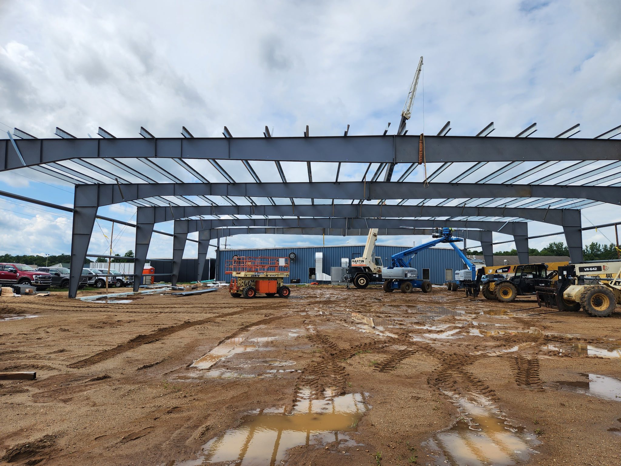 Steel framework of a large building under construction on a muddy site.