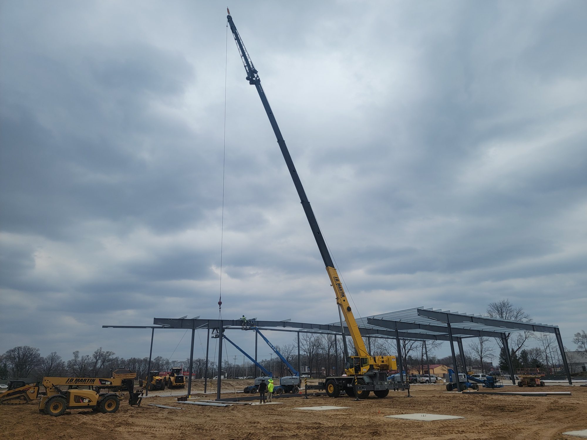 A large crane lifting materials at a construction site under a cloudy sky.