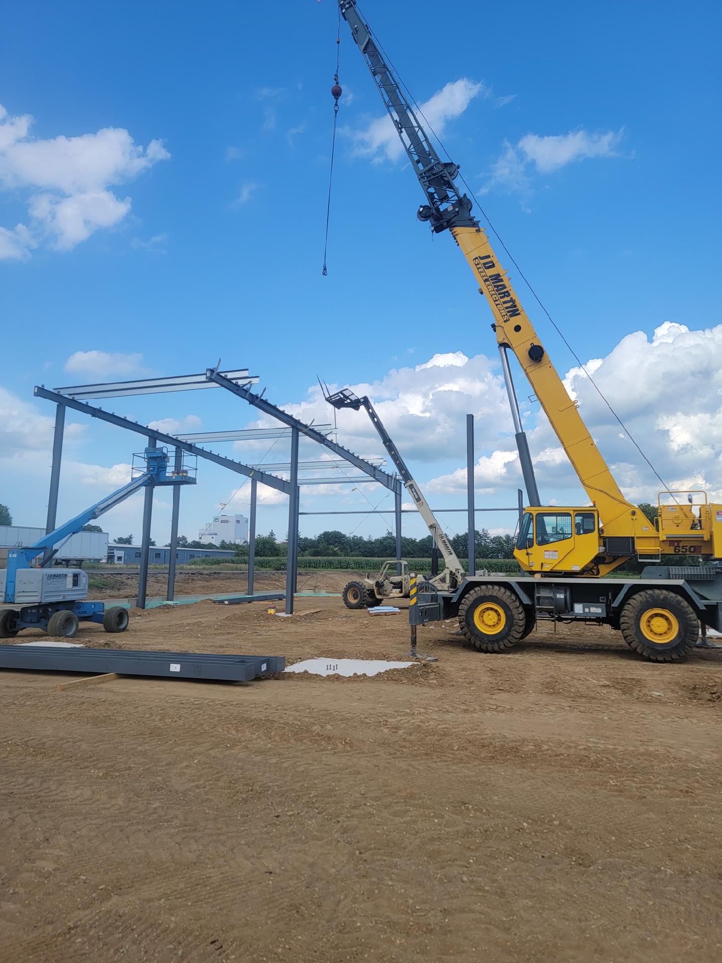 A yellow crane lifting steel beams at a construction site under a blue sky.