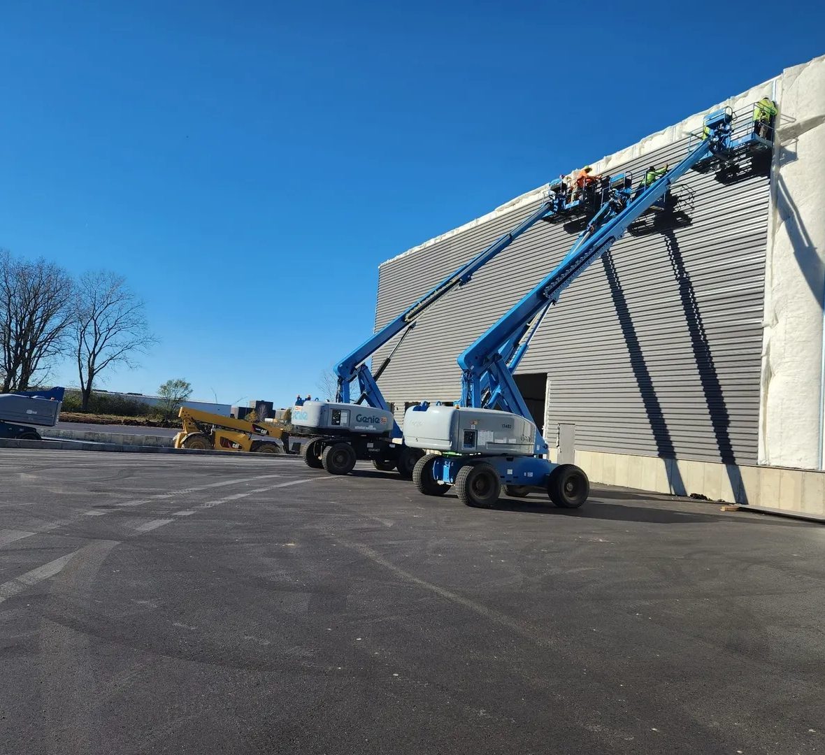 Workers on boom lifts repairing or maintaining a large exterior wall.