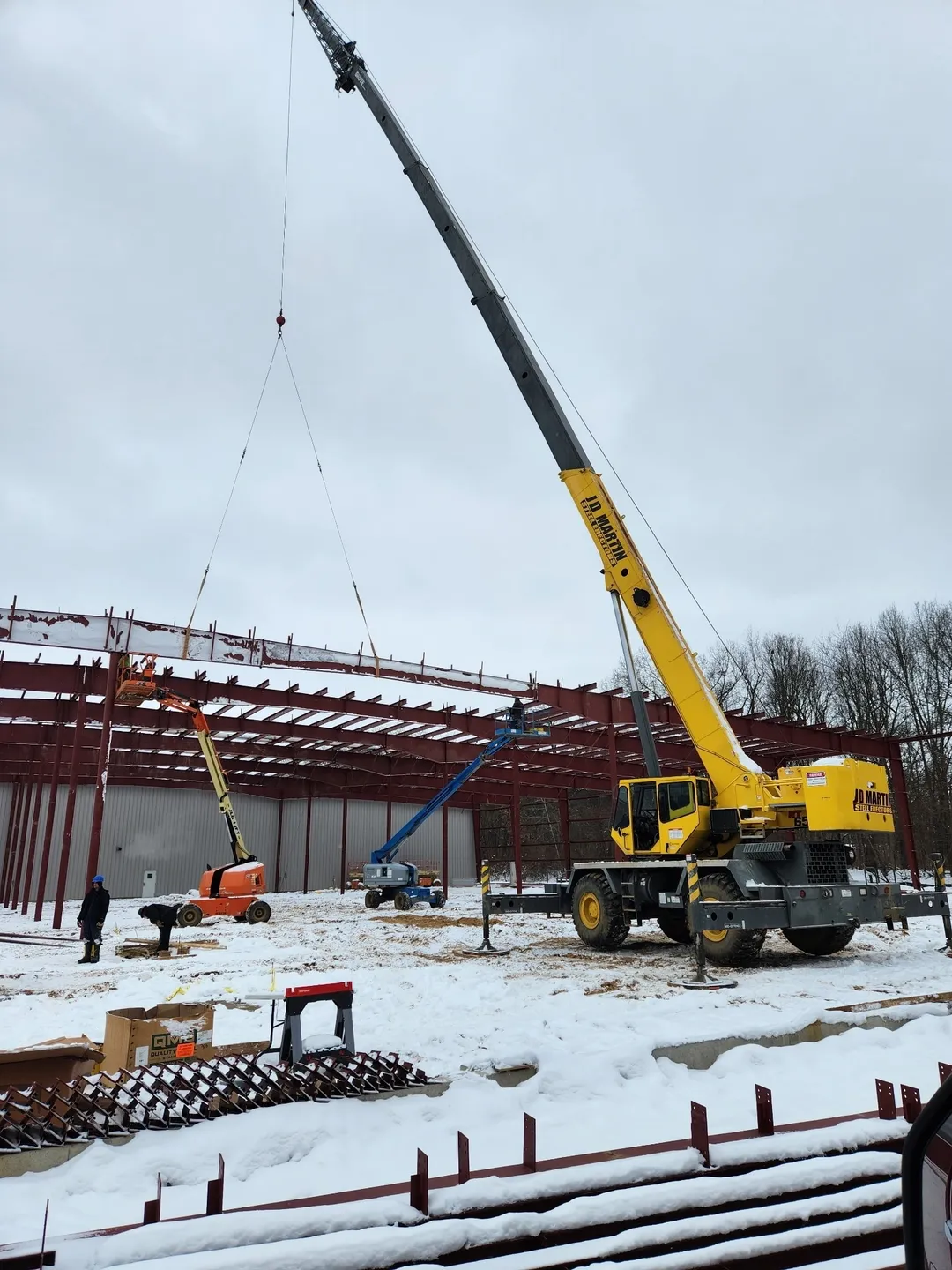 Yellow crane lifting steel beams at a snowy construction site.