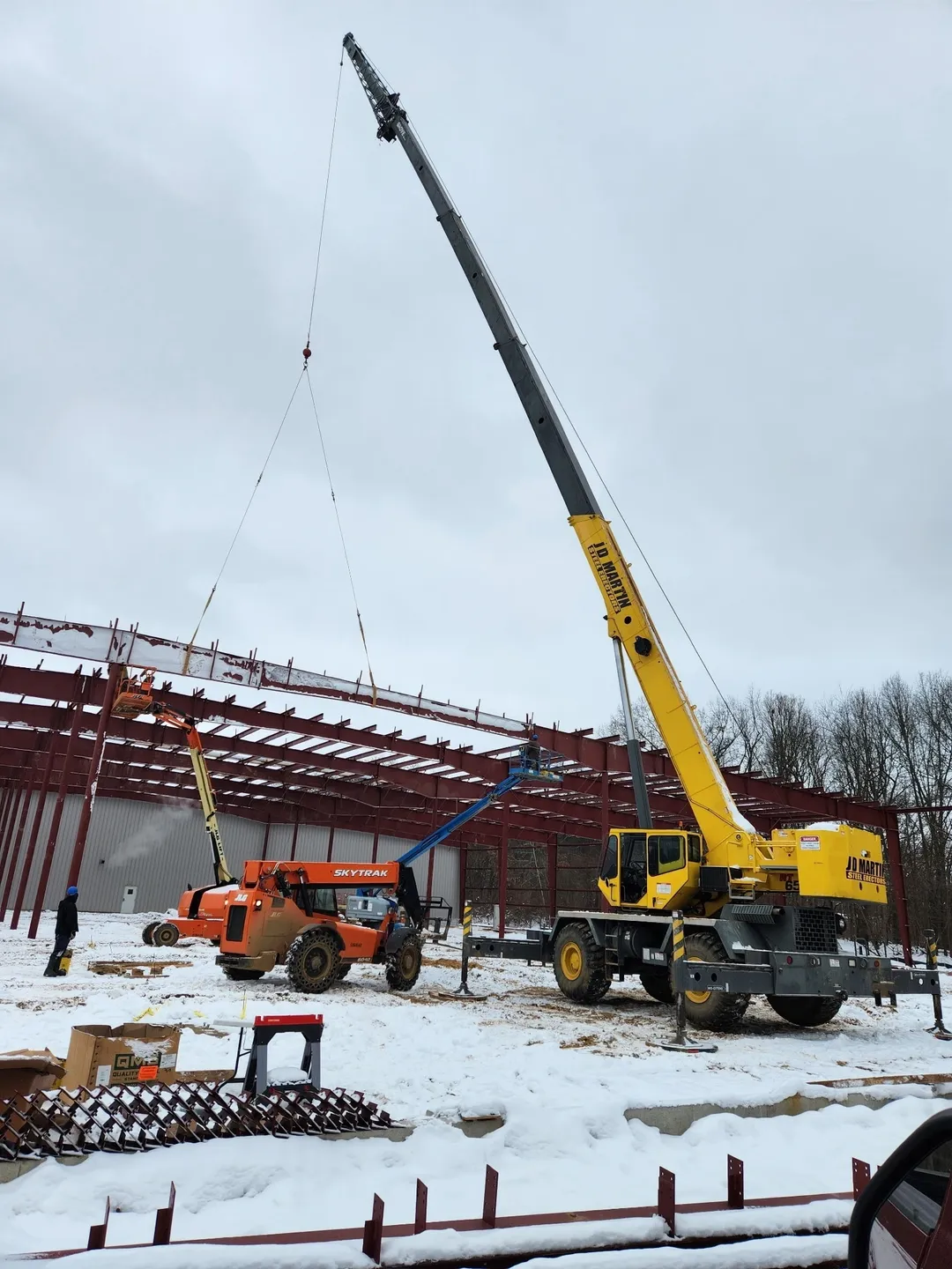 Construction site with cranes assembling steel framework in snowy weather.